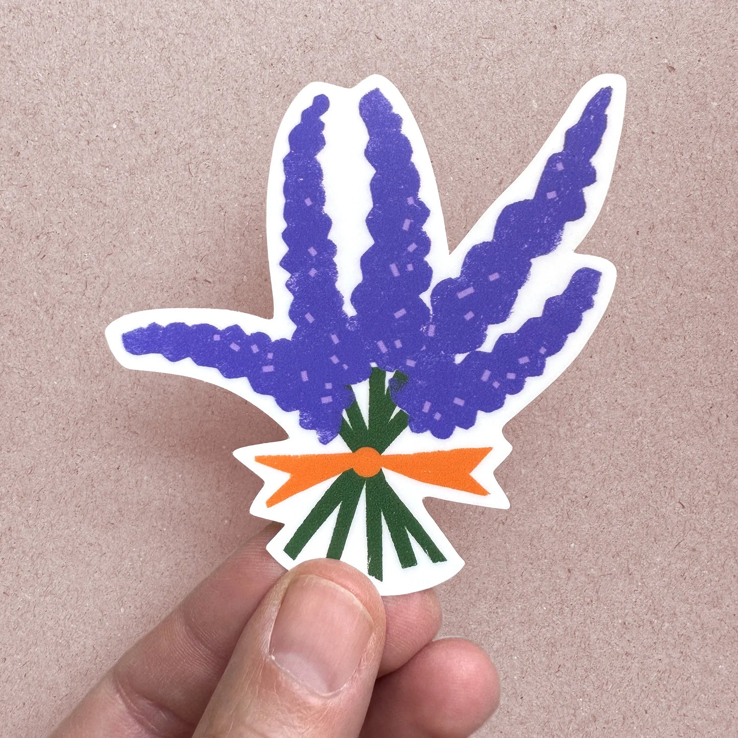 A hand holding a custom-shaped vinyl sticker of a bouquet of wild lupines with green stems and an orange ribbon. The matte sticker is weatherproof and UV-resistant.