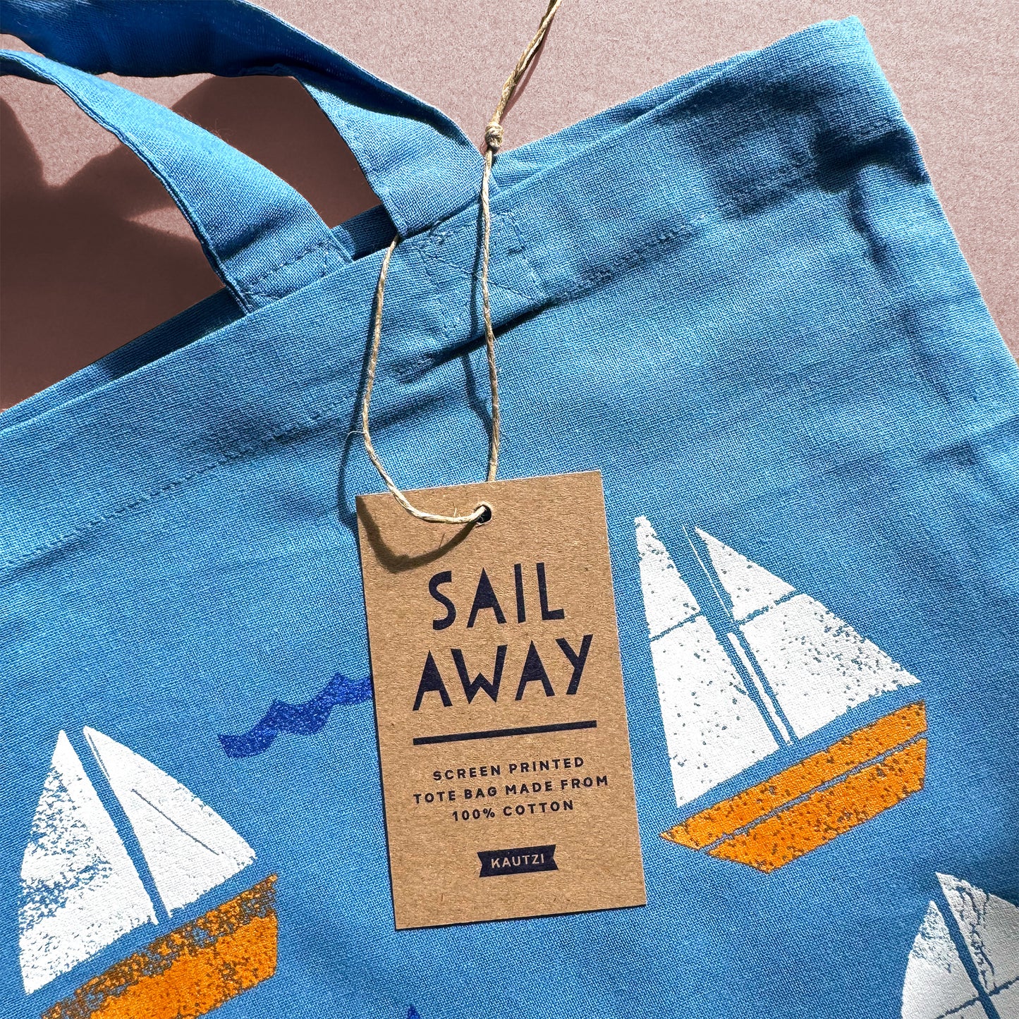 Sail Away Tote Bag featuring white and orange sailboats screen printed on blue cotton fabric with product tag.