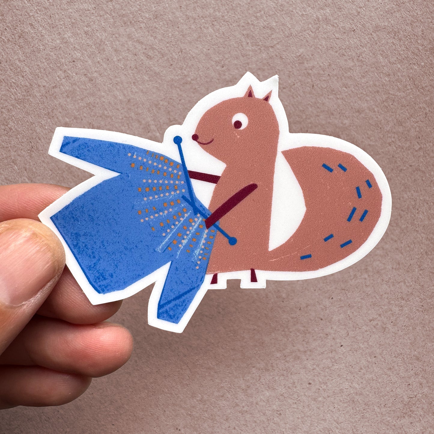 Handheld view of Kautzi Knitting Squirrel sticker – illustrated squirrel with blue sweater, designed in Cape Breton, Canada.