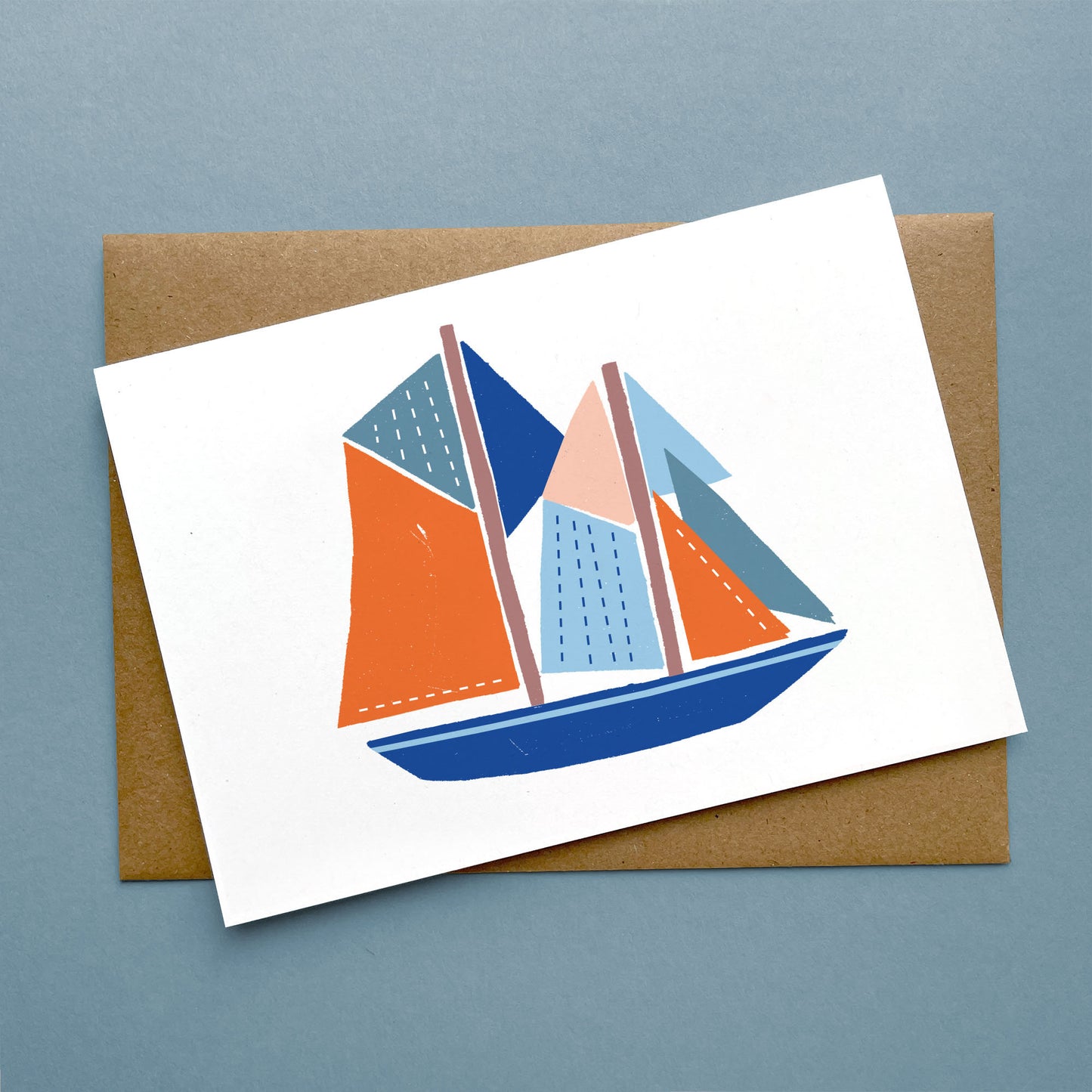 Greeting Card Bluenose features a minimalist paper cut illustration of a blue and orange sailboat on white card with kraft envelope