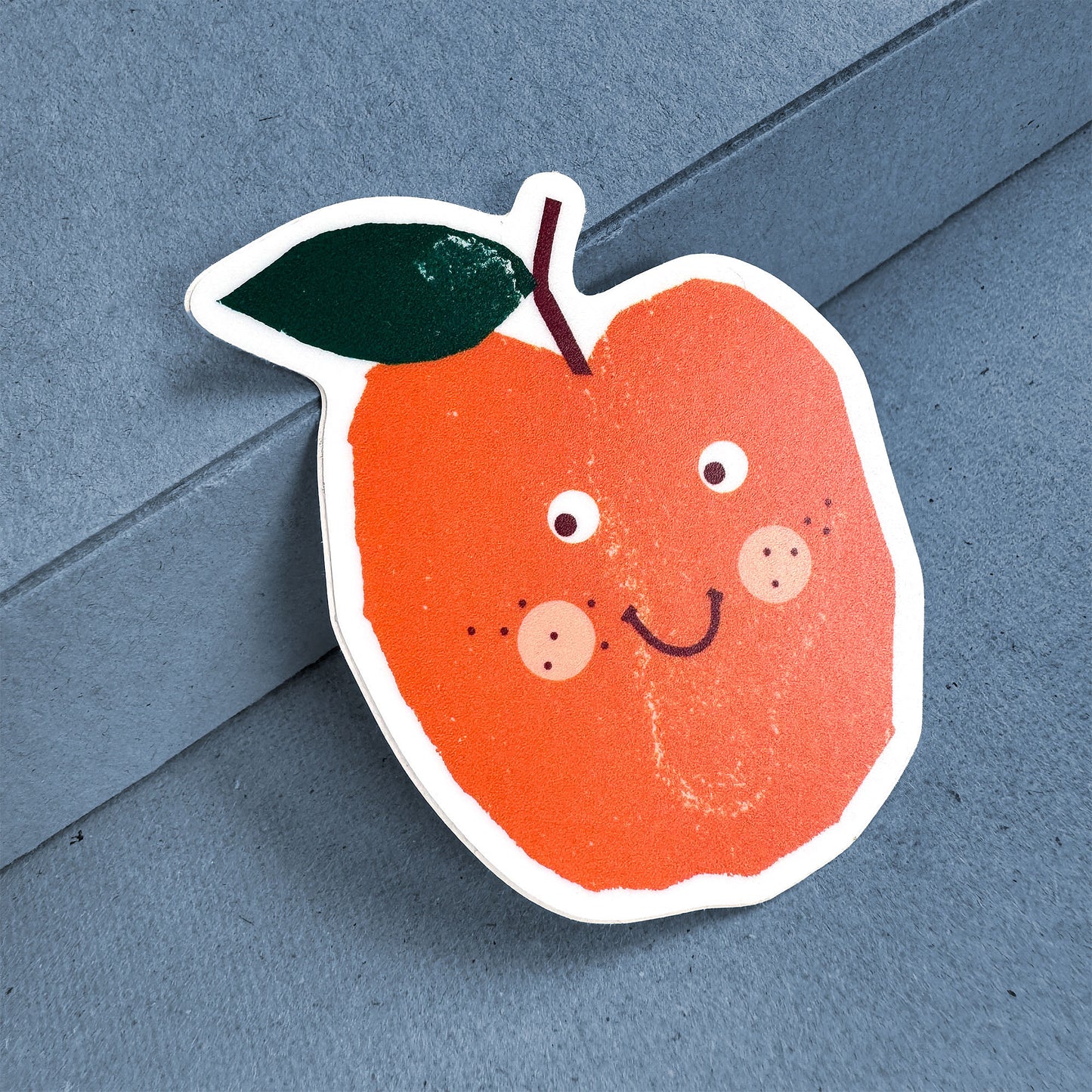 Sticker Apple with cute smiling face design, bright orange color and green leaf on white vinyl background