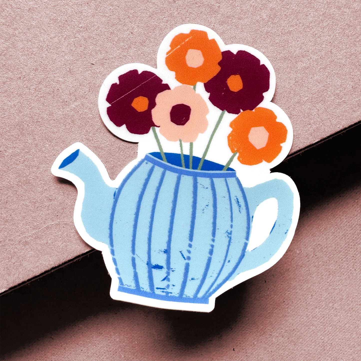 Blue teapot sticker with orange and burgundy flowers, hand-cut paper design style