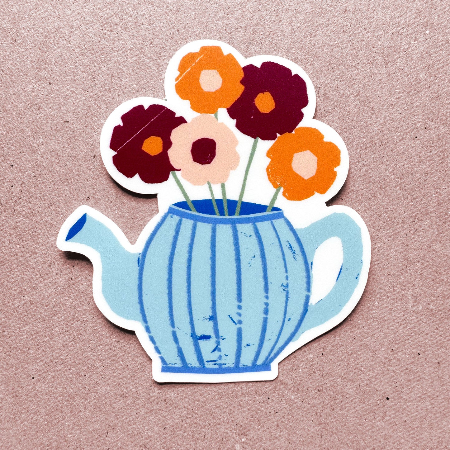 Whimsical blue teapot sticker with burgundy, orange, and peach flowers blooming from spout, handcrafted paper-cut style