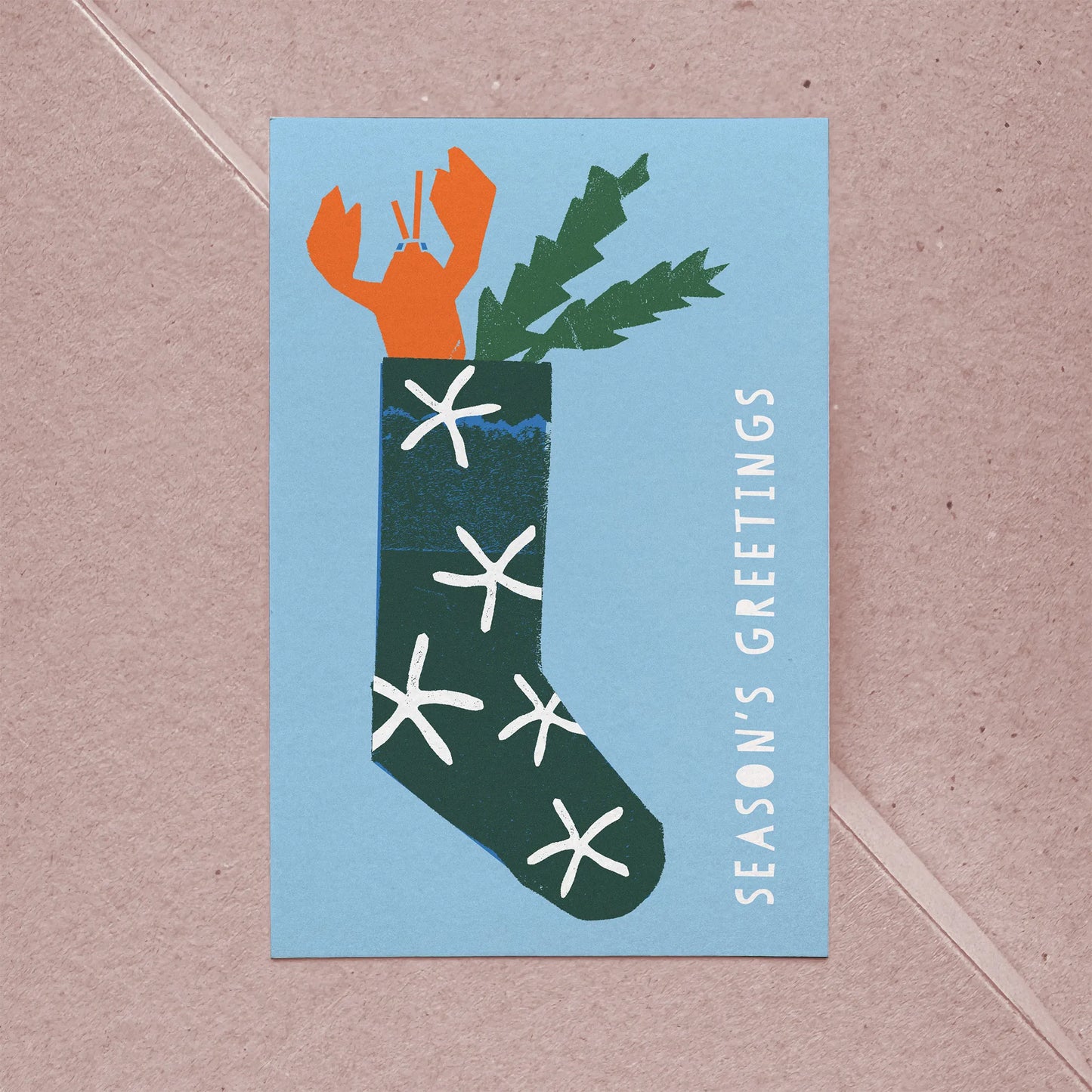 Full front view of festive flat card showing a lobster in a green stocking with white sea star shapes.