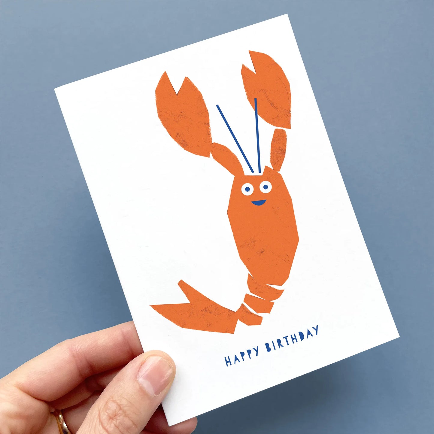 Hand holding a Kautzi lobster birthday card featuring a playful orange lobster illustration and blue “Happy Birthday” text – designed in Cape Breton, Nova Scotia.