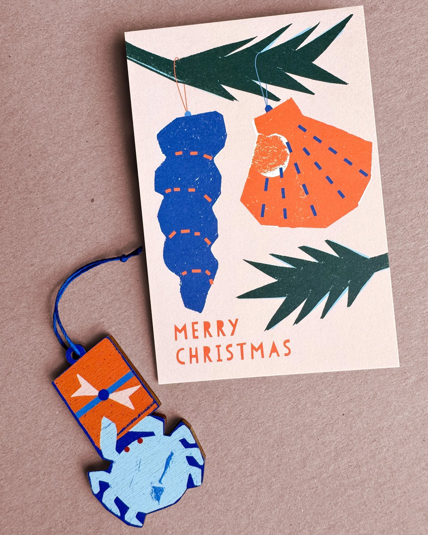 Kautzi crab wooden ornament from Cape Breton, Nova Scotia, shown beside a Merry Christmas card with blue and orange seashell designs.