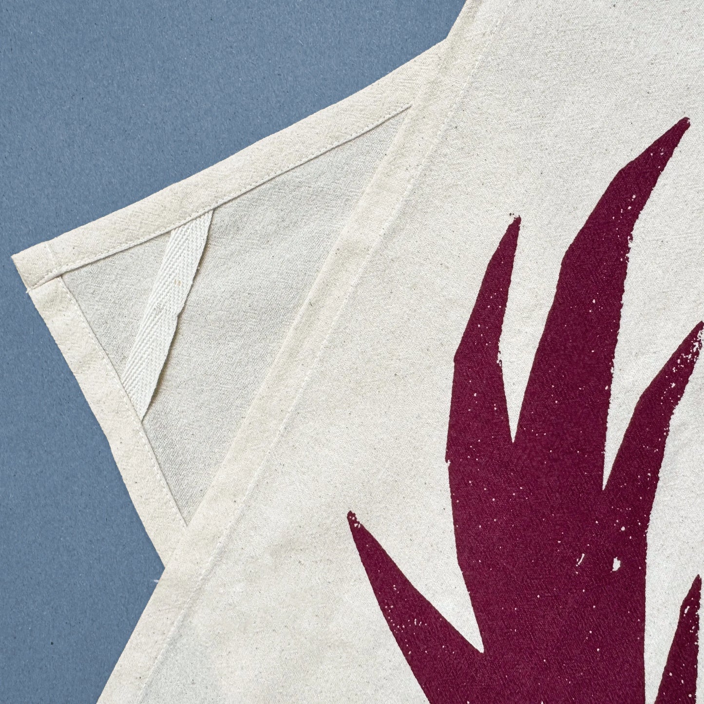 Kautzi Wild Thistles tea towel corner with hanging loop and deep plum thistle motif screen printed on natural cotton.