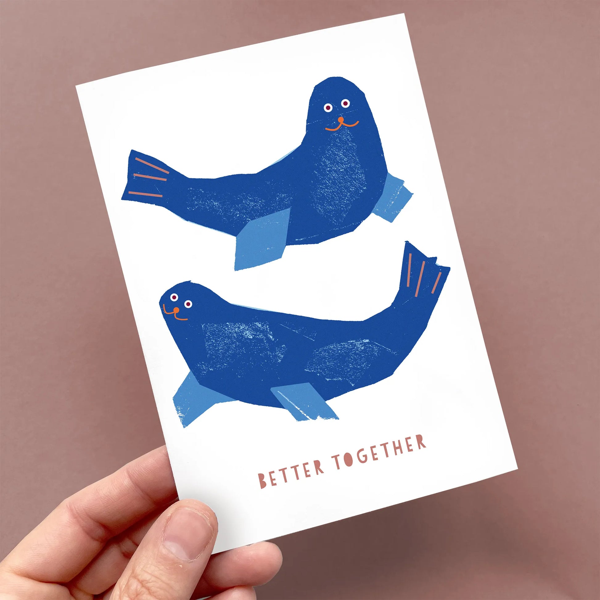 Kautzi greeting card held in hand, showing two blue seals with orange details and the text "Better Together."