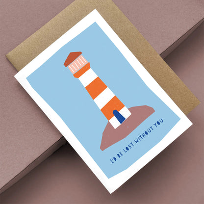 Kautzi greeting card featuring a bold red and white striped lighthouse on a rocky shore with the text "I'd be lost without you," displayed at an angle with a brown kraft envelope.