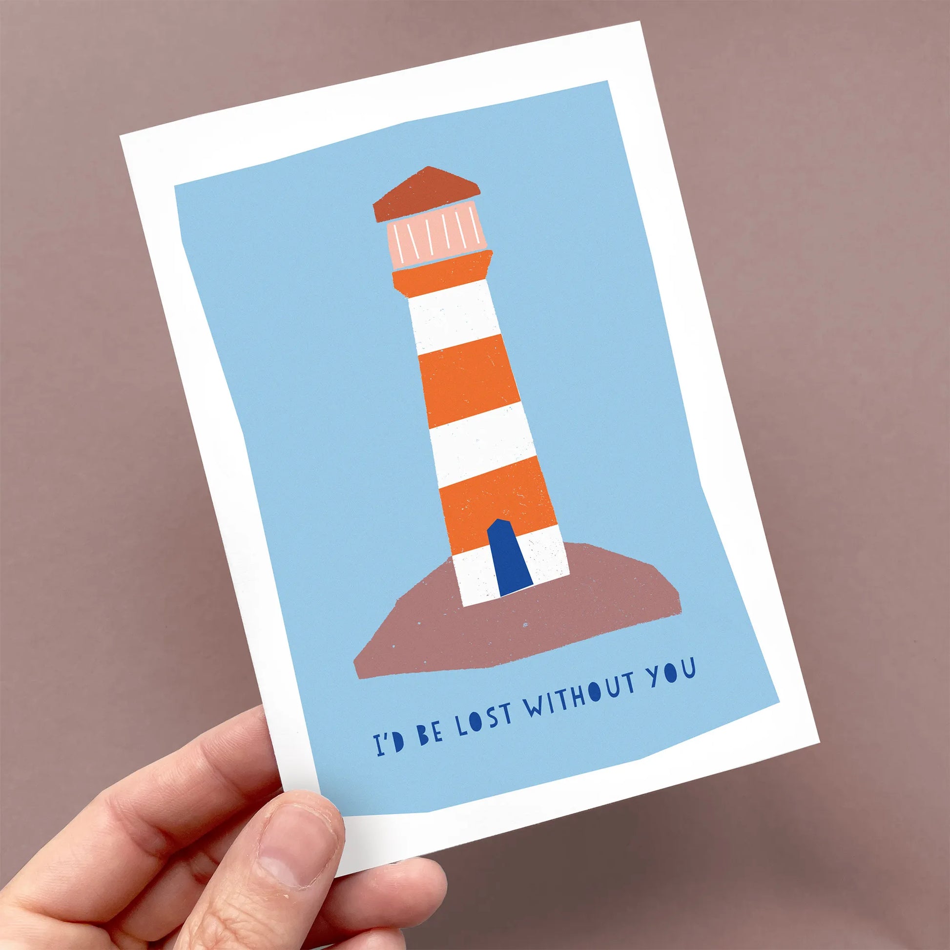 Kautzi greeting card held in hand, showing a red and white lighthouse illustration with the message "I'd be lost without you."