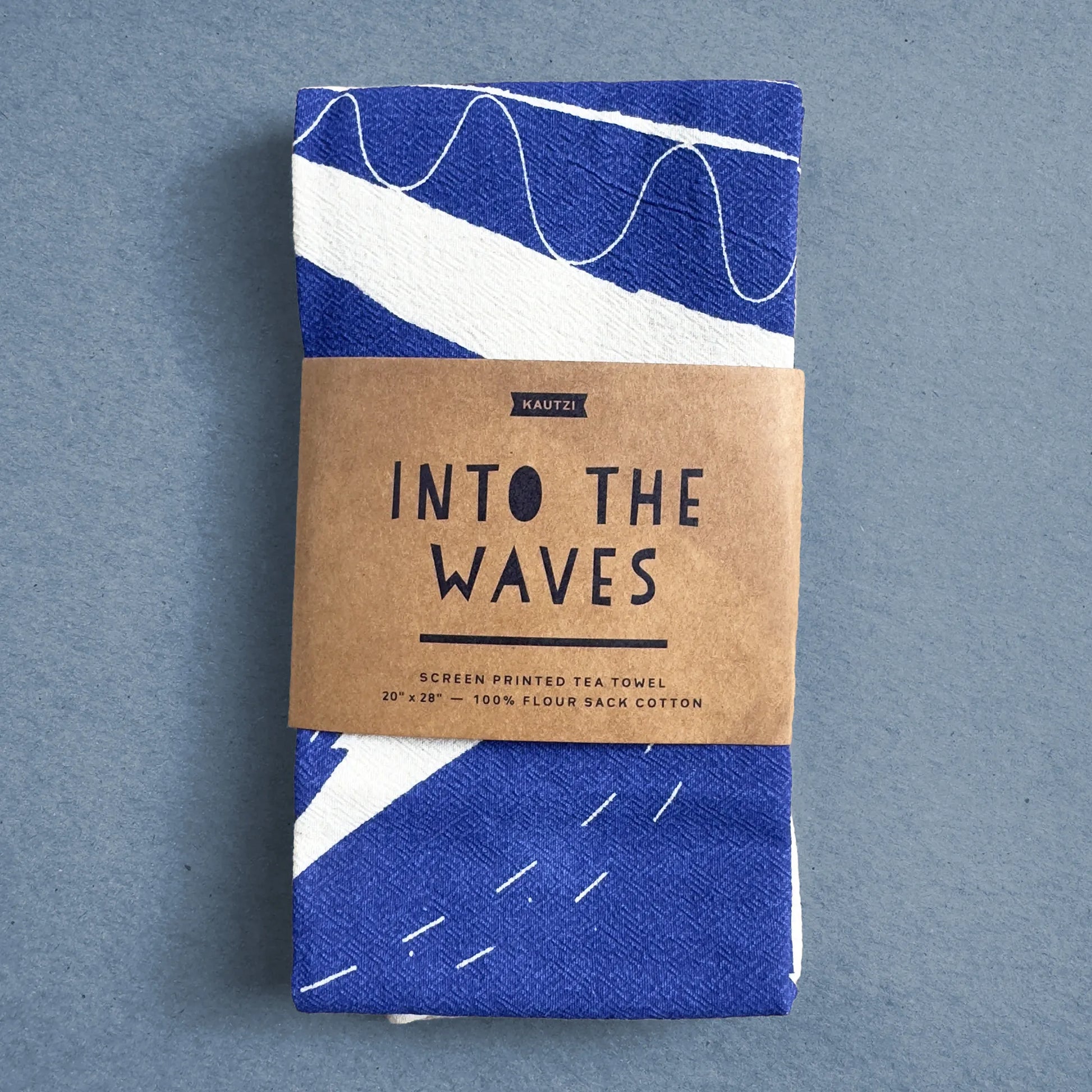 The Into the Waves tea towel by Kautzi, neatly folded and wrapped in kraft paper packaging with the product name and design details.