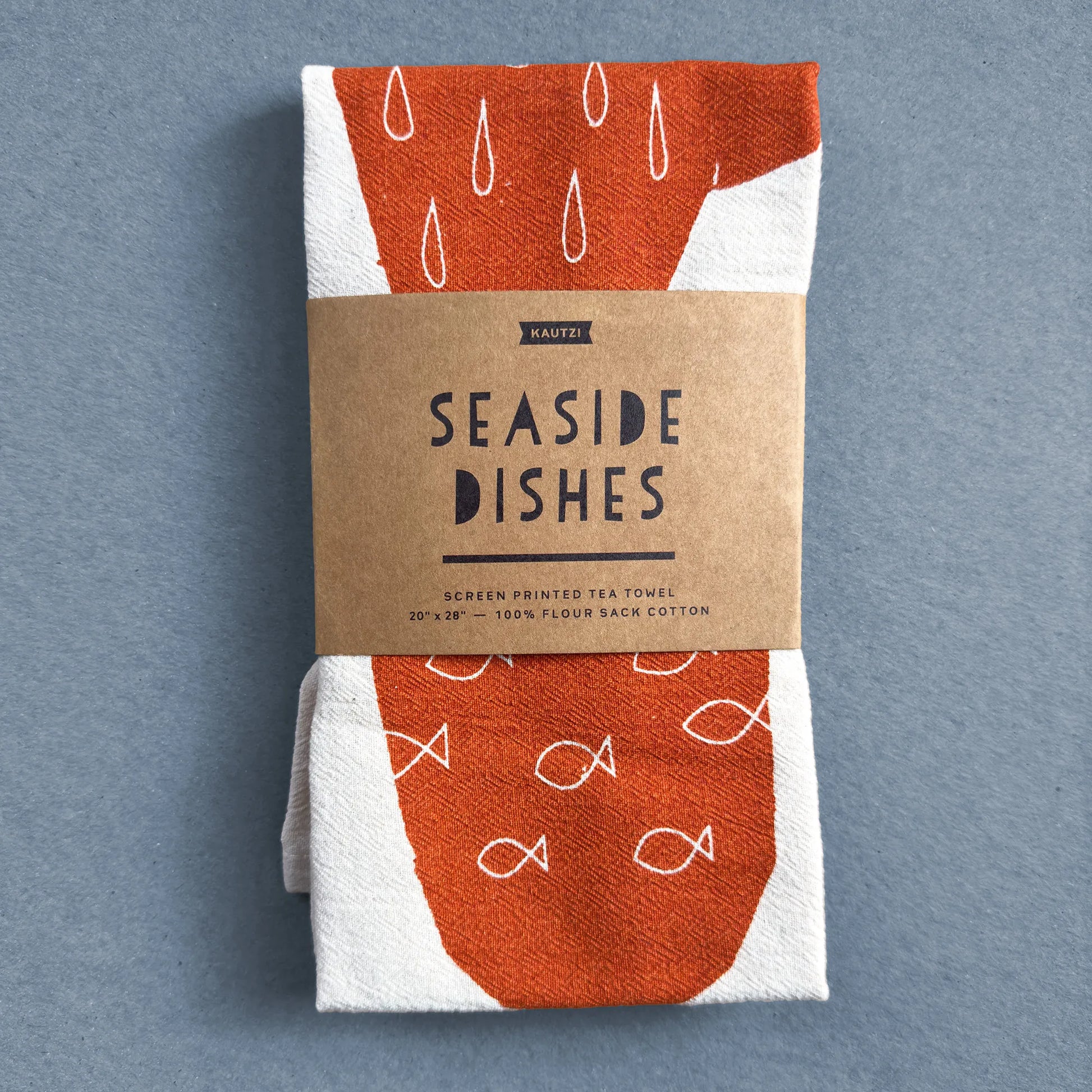 The Seaside Dishes tea towel by Kautzi, neatly folded and wrapped in kraft paper packaging with the product name and description.