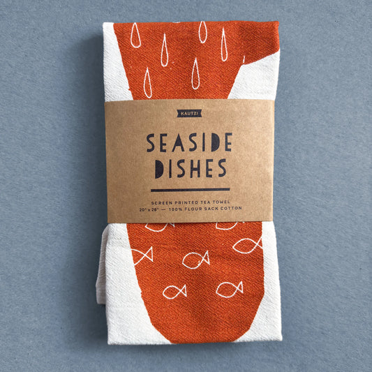 The Seaside Dishes tea towel by Kautzi, neatly folded and wrapped in kraft paper packaging with the product name and description.