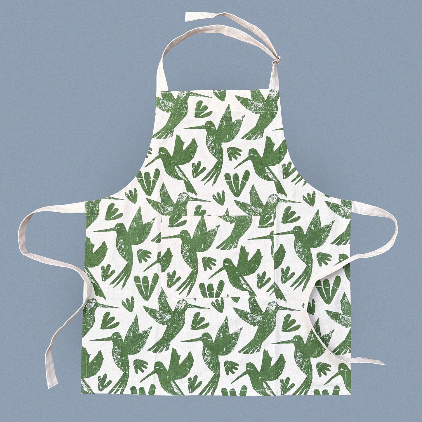 Kautzi Hummingbirds apron laid flat on a soft grey background, screen printed in green on natural cotton with an all-over hummingbird pattern, Cape Breton, Nova Scotia, Canada.