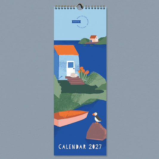 Front cover of the 2027 "Fishing Village" wall calendar by Kautzi, featuring hand-cut paper illustrations of a coastal cove with a blue cottage, sleeping cat, rowboat, and puffin on the rocks, designed in Cape Breton, Nova Scotia. 