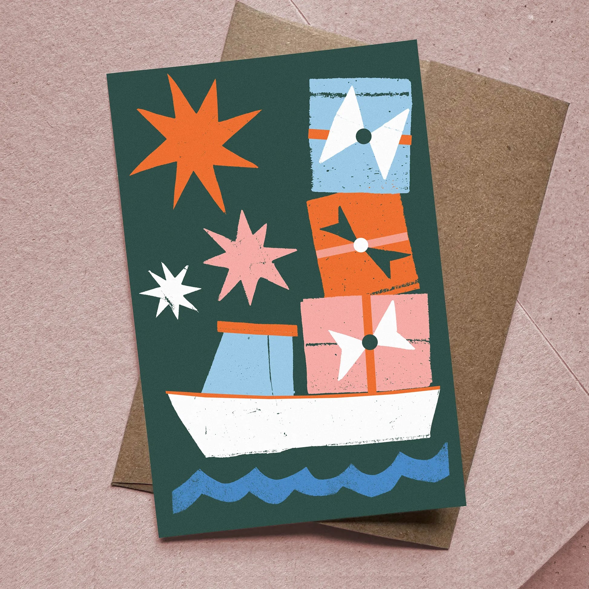 Front of Christmas card titled "Christmas Cargo" showing a lobster boat stacked with gifts and stars, with kraft envelope beneath.