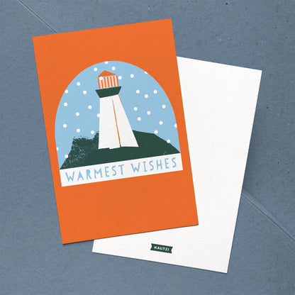 Front and back of the Kautzi Coastal Christmas "Warmest Wishes" holiday  card featuring an illustrated East Coast lighthouse snow globe on a bold orange background. Back shows the Kautzi logo printed on white. Made in Canada.