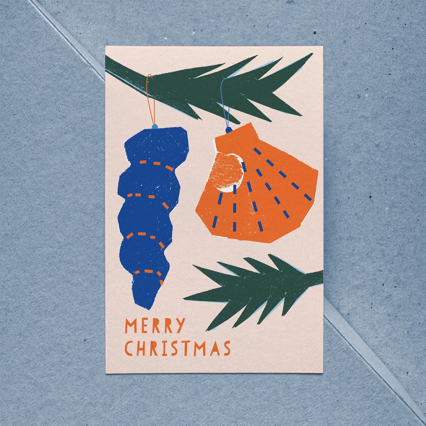 Close-up of flat holiday card showing stylized shell ornaments hanging from spruce branches.