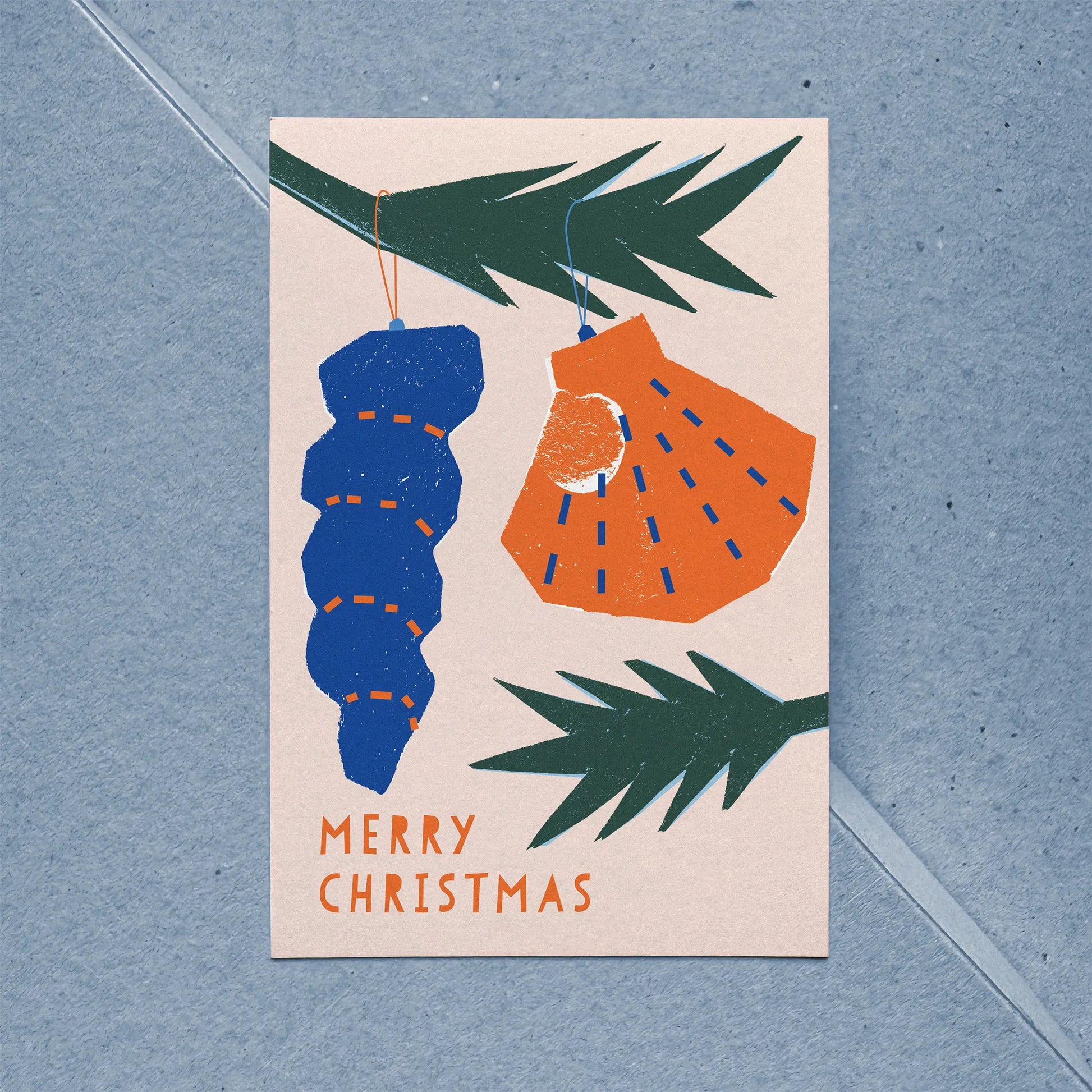 Close-up of flat holiday card showing stylized shell ornaments hanging from spruce branches.