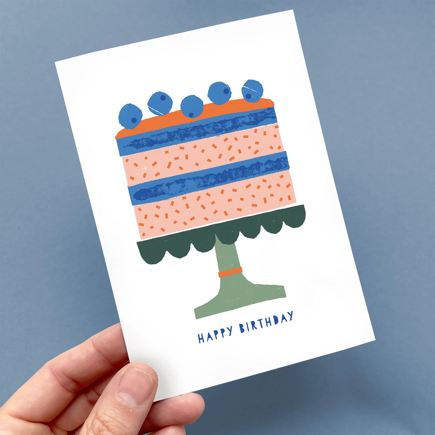Hand holding a Kautzi birthday card featuring a playful illustrated cake with blueberries and “Happy Birthday” text – designed in Cape Breton, Nova Scotia.