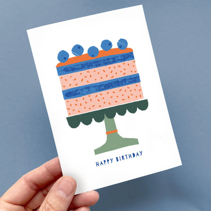 Hand holding a Kautzi birthday card featuring a playful illustrated cake with blueberries and “Happy Birthday” text – designed in Cape Breton, Nova Scotia.