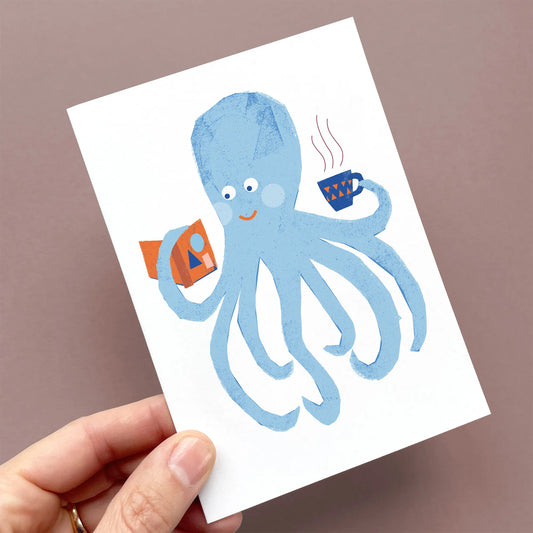 Hand holding a Kautzi greeting card featuring a friendly blue octopus enjoying a hot drink and a good book – designed in Cape Breton, Nova Scotia.