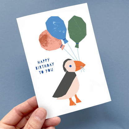 Kautzi puffin birthday greeting card held in hand, playful balloon illustration, designed in Cape Breton, Nova Scotia, Canada