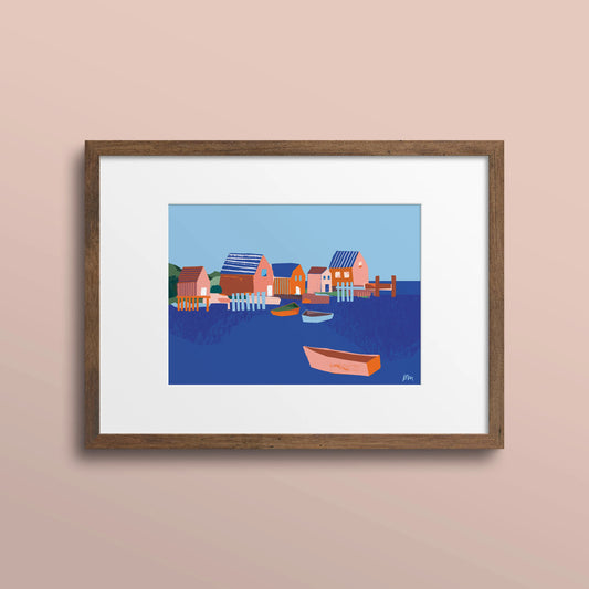 Framed 5x7 art print of colourful fish shacks and boats in a Nova Scotia harbour, shown with a white mat and wood frame on a pale pink wall.