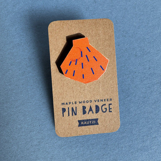 Kautzi maple wood veneer shell pin badge on kraft display backing, orange with blue accents, coastal-inspired accessory