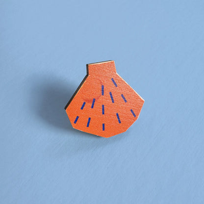Close-up of Kautzi maple wood veneer shell pin badge in bright orange with blue lines, inspired by Nova Scotia shoreline finds