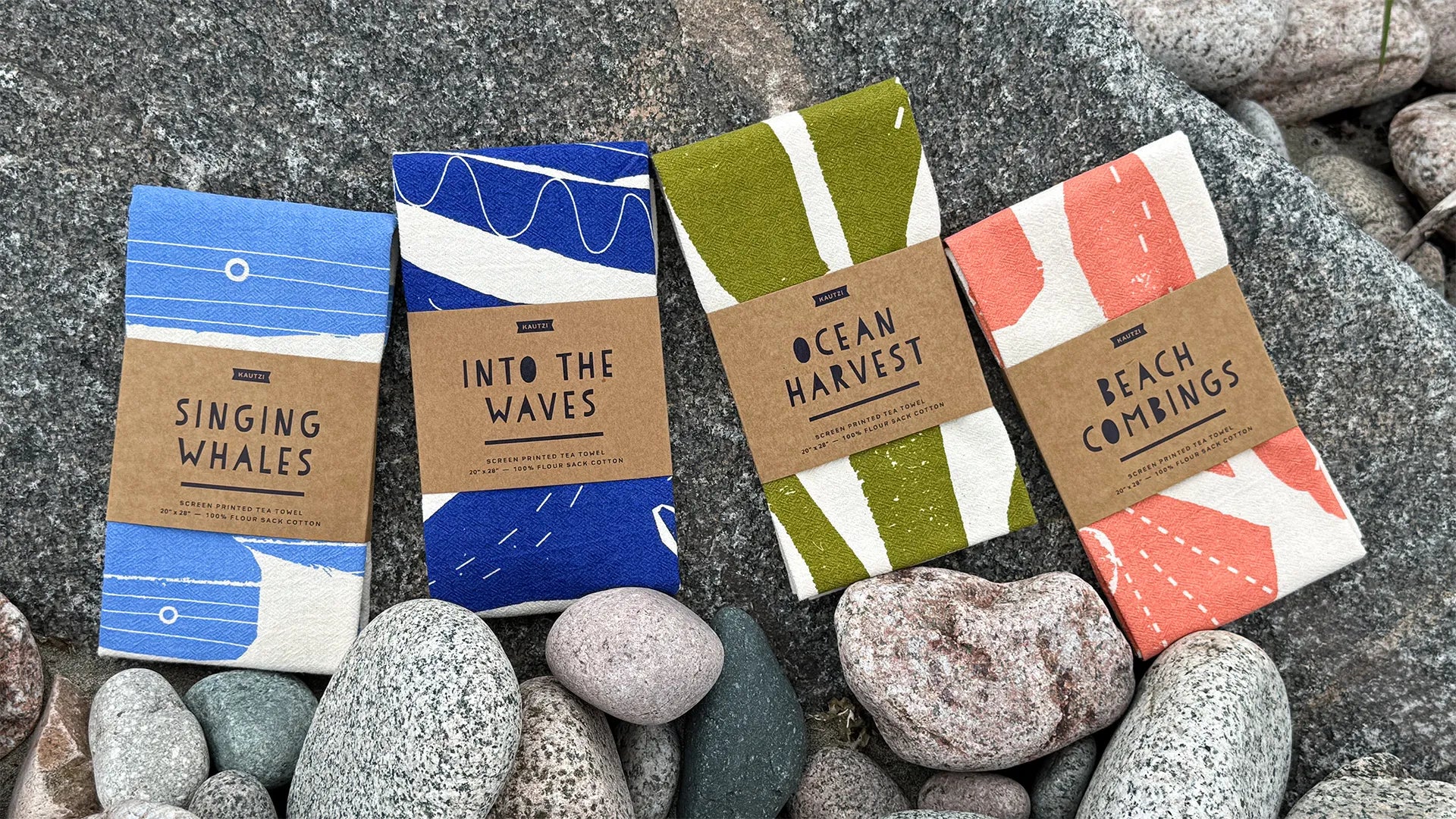Four screen-printed Kautzi tea towels – Singing Whales, Into the Waves, Ocean Harvest, and Beach Combings – displaying hand-cut Maritime designs on coastal rocks, designed in Cape Breton, Nova Scotia