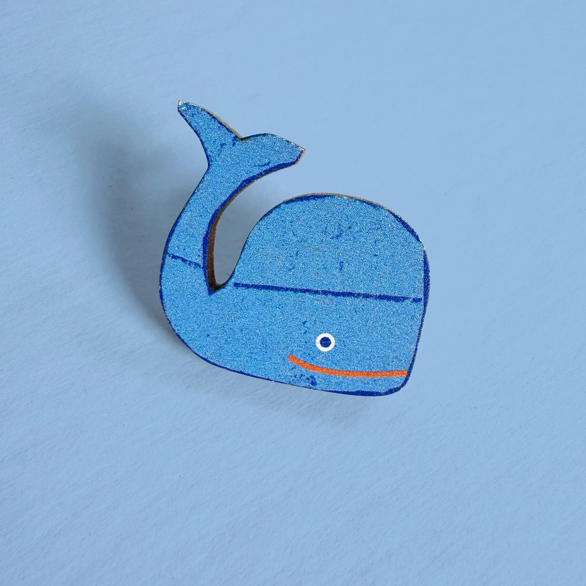 Close-up of Kautzi maple wood veneer whale pin badge in bright blue with orange smile, inspired by Nova Scotia marine life