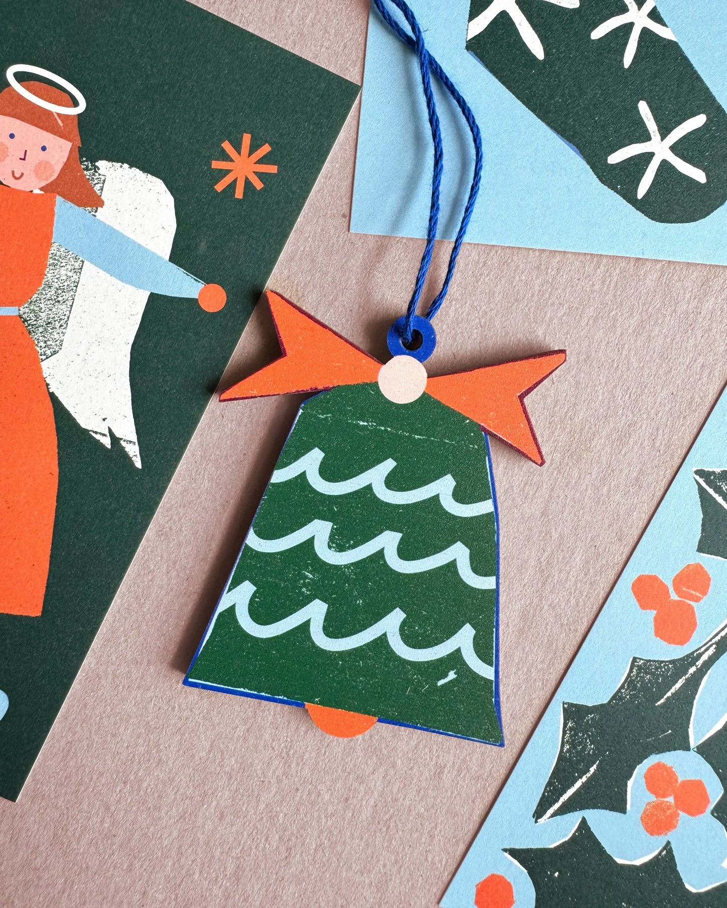 Kautzi sea bell wooden ornament displayed with holiday cards in coastal colours of green, blue, and orange.
