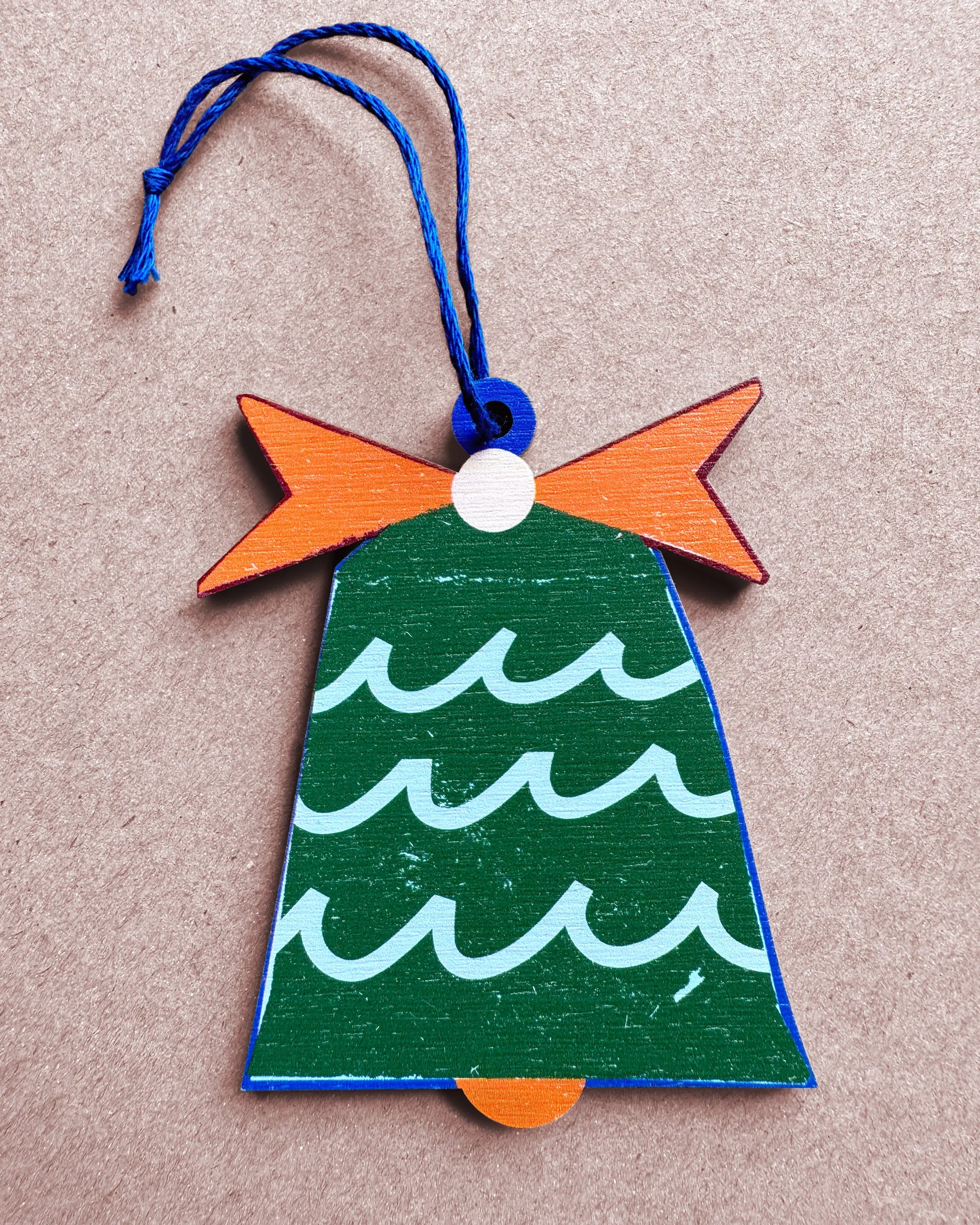 Flat lay of the Kautzi sea bell wooden ornament with wave pattern and orange bow, designed in Cape Breton, Canada.