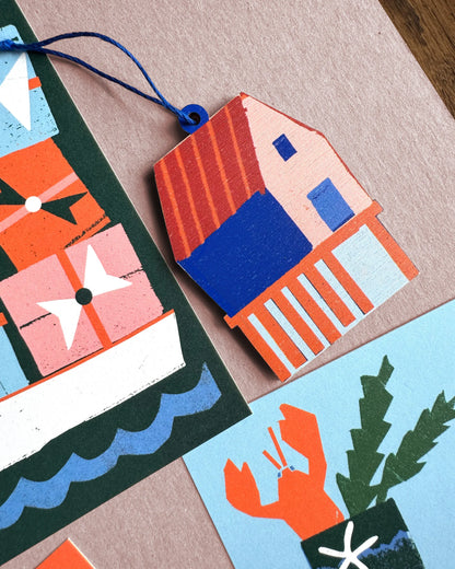 Kautzi fish shack wooden ornament paired with coastal holiday cards in blue, green, and orange tones.