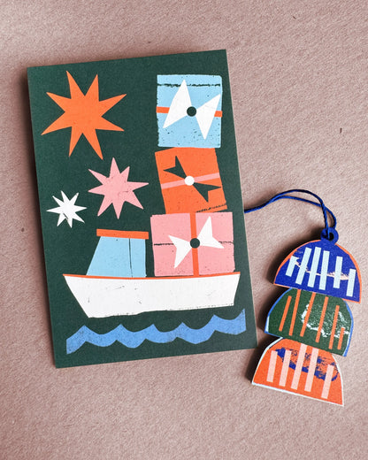 Kautzi lobster trap wooden ornament from Cape Breton, Nova Scotia, shown next to a Christmas card with a lobster boat carrying gift boxes.