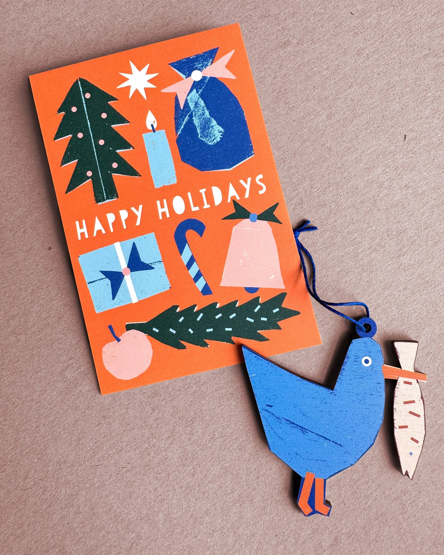 Kautzi seagull wooden ornament from Cape Breton, Nova Scotia, shown beside a Happy Holidays card in blue and orange tones.