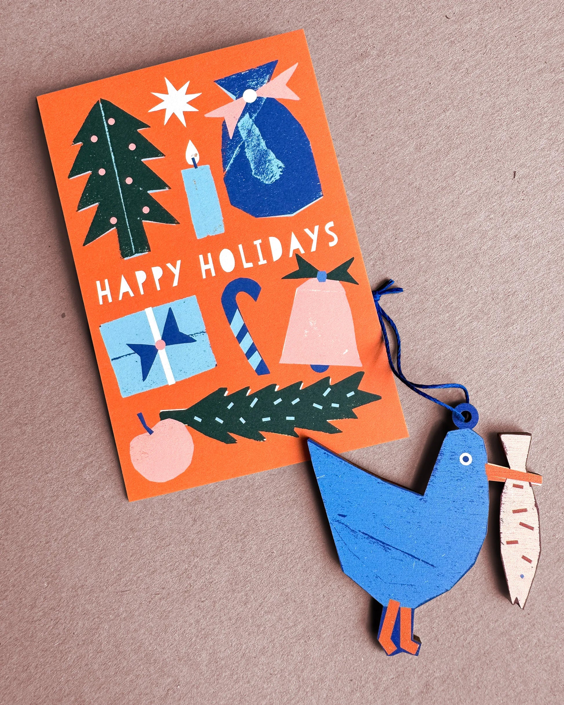 Kautzi seagull wooden ornament from Cape Breton, Nova Scotia, shown beside a Happy Holidays card in blue and orange tones.