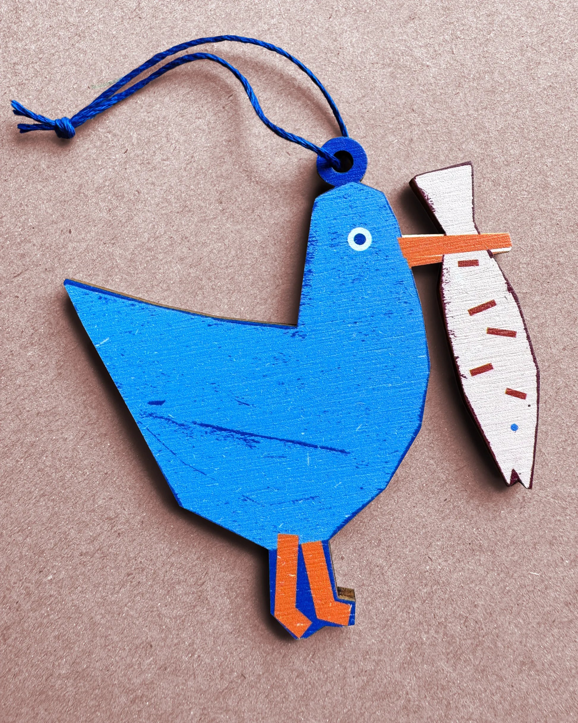 Flat lay of a blue seagull wooden ornament holding a fish, designed by Kautzi in Cape Breton, Nova Scotia.